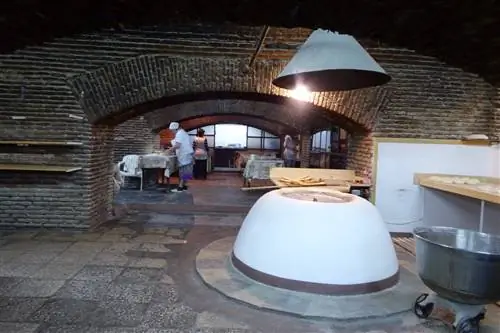 Большая пекарня с открытыми кирпичными стенами и несколько пекарей на заднем плане.