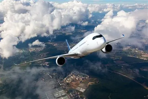 Белый пассажирский самолет поднимается сквозь облака. Самолет летит высоко над городом.