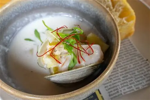 Глазурованная керамическая миска с похлебкой из моллюсков в Union в Портленде, штат Мэн, представляет собой легкий белый бульон, на фоне которого выделяются микрозелень и ярко-красные нити шафрана, когда они драпируют моллюска, все еще в раковине.