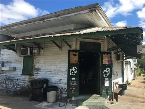 Внешний вид бара Bj. Пара зеленых дверей с логотипом Bj открыта и ведет в бар. Вокруг бара стоит ржавый навес.