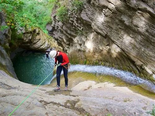 Человек, одетый в черное и красное и в защитном снаряжении, готовится к спуску в каньон Фурко в Пиренеях.