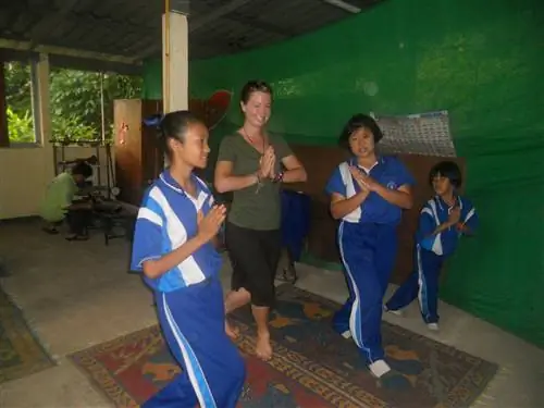Писатель-эколог Британи Робинсон стоит с тремя тайскими девочками разного возраста. Девушки в синих спортивных костюмах, сжав ладони вместе. Британи в зеленом топе и черных штанах в похожей позе.