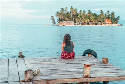 Женщина сидит на причале в Таиланде, любуясь голубым океаном. Остров находится в поле зрения.