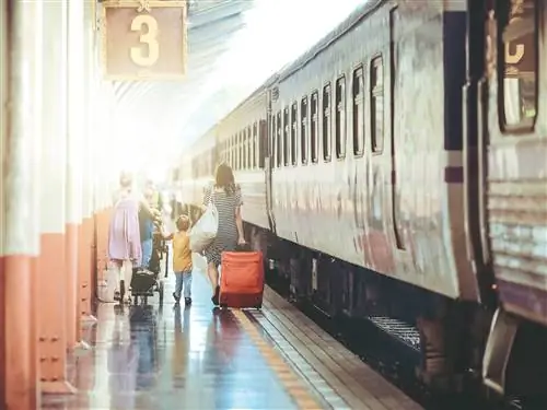 Семейная группа идет по платформе. Одна женщина толкает коляску с ребенком на спине, другая тащит чемодан на колесиках. Рядом с ними идет еще один ребенок