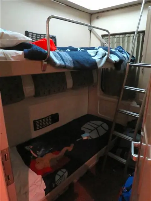 Две койки в маленьком купе поезда с лестницей из нержавеющей стали в конце