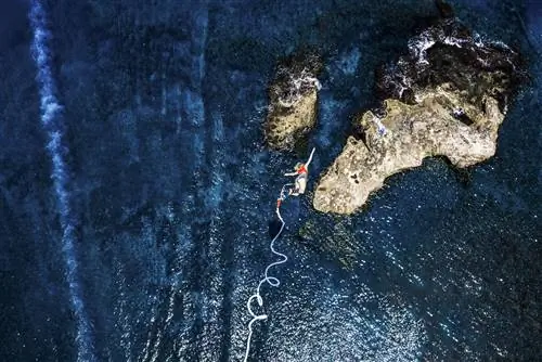 Вид сверху вниз на женщину, прыгающую с банджи над синим морем в Греции.