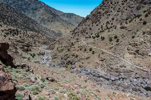 Одноколейная пешеходная тропа извивается вдоль крутого склона скалистой долины по пути к Джебель-Тубкалю; долина бесплодна, на склонах разбросаны лишь небольшие кустарники.