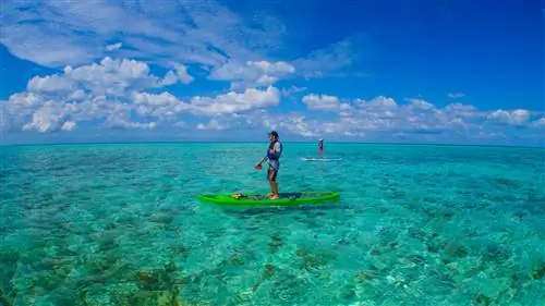 Два человека, разделенные 20-30 метрами, стоят на байдарках над лазурной водой, над которой голубое небо.