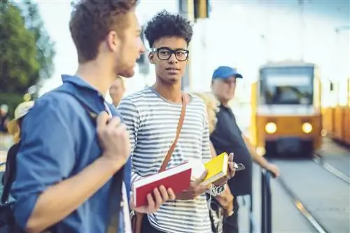 Двое молодых мужчин стоят на трамвайной остановке, когда приближается желтый трамвай.