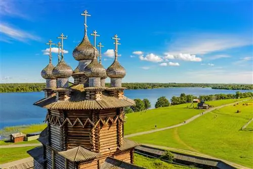 Многокупольная деревянная башня с крестом на каждом куполе, расположенная в травянистом поле на берегу озера.