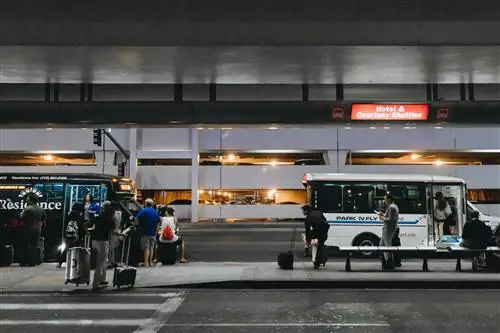 Прибывающие выстраиваются в очередь на автобусных остановках, чтобы сесть на бесплатные автобусы до отелей в аэропорту ночью.