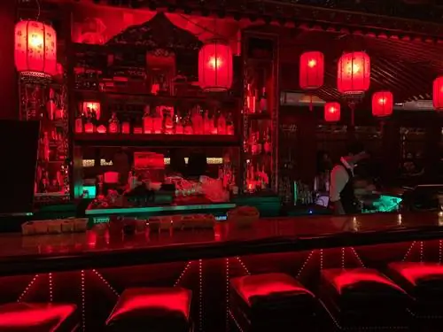 Красные бумажные фонари свисают с потолка бара в The Cafe Formosa, заливая красным светом всю территорию. Рядом работает бармен.