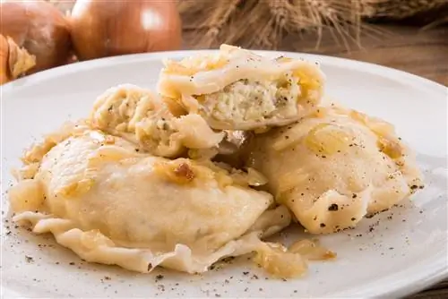 Крупный план тарелки пельменей, фаршированных сыром, покрытых черным перцем и жареным луком.
