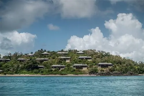 Виллы в элитном курорте Qualia Beach Resort с частным пляжем, построенном на зеленом холме с видом на коралловое море. Голубое небо с белыми облаками.