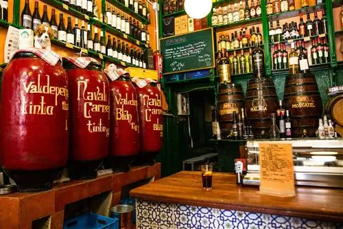 Интерьер Bodegas Ricla, Мадрид; вдоль стен стоят чаны с вином, над которыми зеленые полки, забитые винными бутылками.