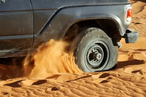 Переднее колесо Toyota Land Cruiser крутится в глубоком песке, разбрасывая его повсюду. Переднее колесо Toyota Land Cruiser крутится в глубоком песке, разбрасывая его повсюду.