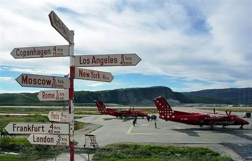 Знак, указывающий на ряд международных направлений, включая Копенгаген, Лос-Анджелес и Лондон, на фоне красных самолетов Air Greenland на фоне скал в Кангерлуссуаке, Гренландия.