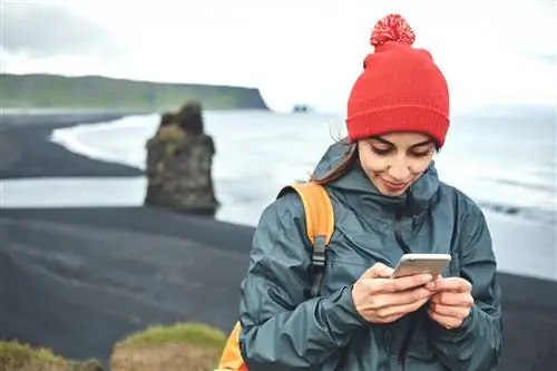 Женщина в ярко-красной шляпе разговаривает по телефону на черном пляже в Исландии.