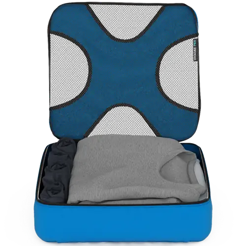 Показан синий упаковочный куб с открытой сетчатой крышкой, отмеченной большой синей Х-образной панелью. Внутри сложена одежда нейтральных цветов, в том числе серый свитер.