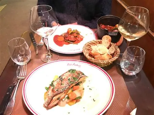 Два основных блюда и два бокала белого вина на маленьком столике.