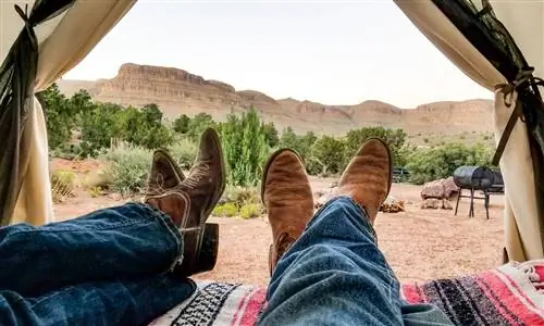 Две пары ног в ковбойских сапогах скрещены под проемом палатки, вид на запад снаружи.