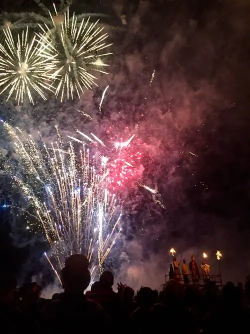 Ночная сцена фейерверков, освещающая темное небо. Головы стоящих в толпе людей вырисовываются на фоне яркого фейерверка.