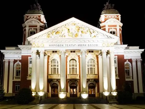 Внешний вид большого красного здания с колоннами в греческом стиле в ночное время.