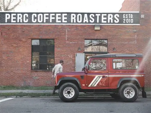 Красный Land Rover Defender припаркован перед красным кирпичным фасадом кофейни Perc Coffee Roasters.