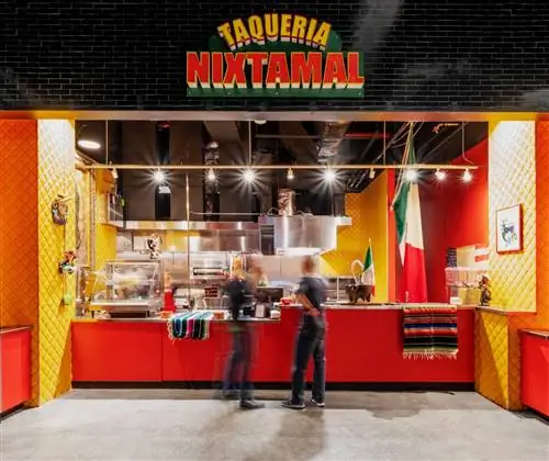 Витрина магазина Taqueria Nixtamal - ярко-красная прилавок, желто-красные стены, справа висят мексиканские флаги.