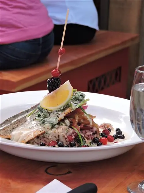 Кусок лосося, проткнутый деревянной палочкой с долькой лимона и ягодами, лежит на подушке из риса, смешанного с ягодами; Местная еда