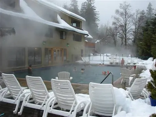 Пар поднимается на фоне серого неба и заснеженной крыши курорта Belknap Hot Springs Resort, пока купальщики наслаждаются голубыми водами бассейна, окруженного пластиковыми шезлонгами, белыми, как снег.