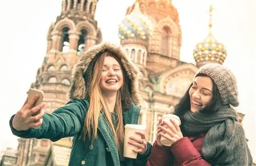 Две смеющиеся девушки делают зимнее селфи у церкви в Санкт-Петербурге.