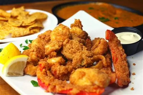 Крупный план тарелки жареной курицы на сейтане с жареным красным перцем. На заднем плане тарелка с чипсами и соусом; Веганский ресторан в районе залива Сан-Франциско