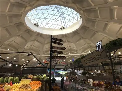 Изогнутый потолок со стеклянным куполом в центре; слева есть фруктово-овощной прилавок, а справа ряд других рыночных прилавков Изогнутый потолок со стеклянным куполом в центре; слева есть фруктово-овощной прилавок, а справа ряд других рыночных прилавков