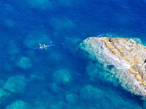 Одиночный каякер, окруженный глубоким синим морем и единственным скалистым обнажением; если смотреть сверху.