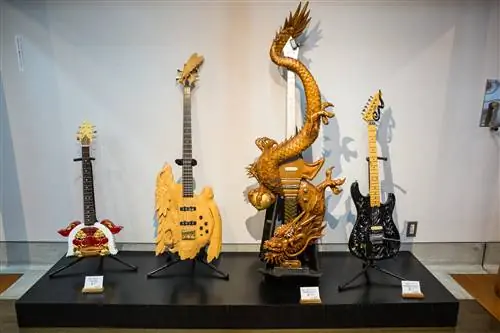 Четыре электрогитары опираются на подставки, каждая из которых украшена замысловатыми деревянными узорами. Один из них представляет собой тщательно продуманного дракона, который проходит по грифу гитары.