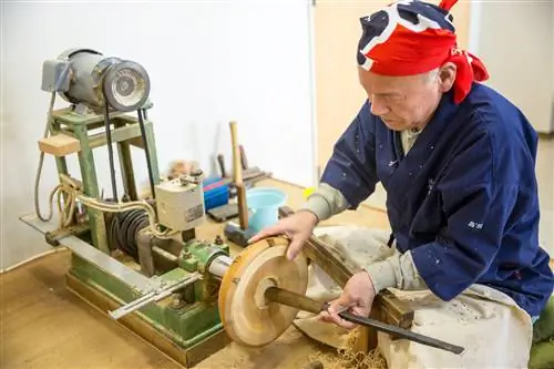 Мастер в синем комбинезоне и бандане склоняется над инструментами, из которых видно дно чаши.