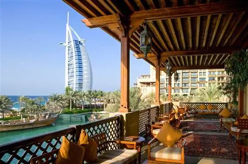 Ресторан с видом на Burj Al Arab в Дубае. Фотография сделана с лакированного деревянного балкона, украшенного ткаными ковриками и деревянными мягкими сиденьями.