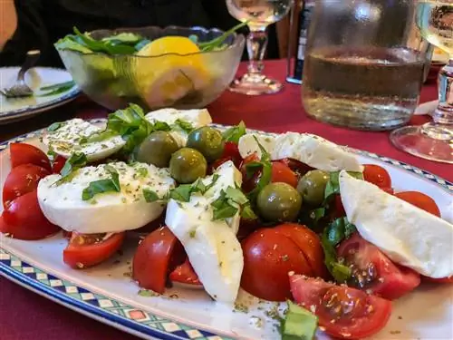 Салат Капрезе с сыром моцарелла, помидорами, базиликом и оливками на столе на острове Искья, Кампания, Италия.