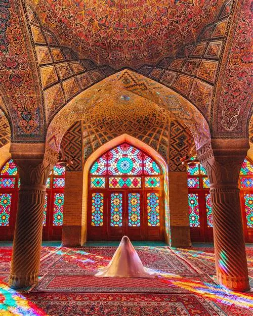Симметрия отлично смотрится в Instagram; внутри красочной мечети Насир-ол-молк в Иране; красная ковровая дорожка с замысловатым узором, а колонны поддерживают сводчатый потолок, украшенный удивительно детализированной плиткой. В центре кто-то молится, накрытый белым покрывалом.