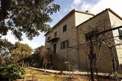 Трехэтажное каменное здание Casa Robert Graves расположено в саду, полном деревьев.