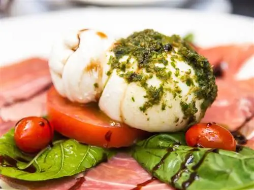 Шарик белого сыра лежит поверх помидора и вяленого мяса.