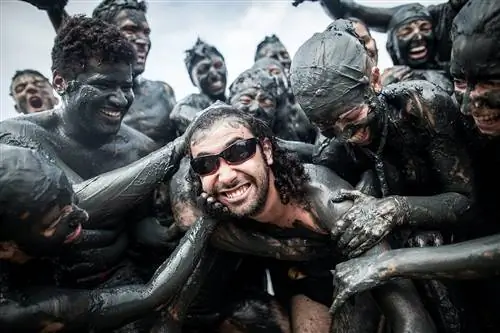 Десятки посетителей карнавала вымазывают мужчину в темных очках темной грязью.