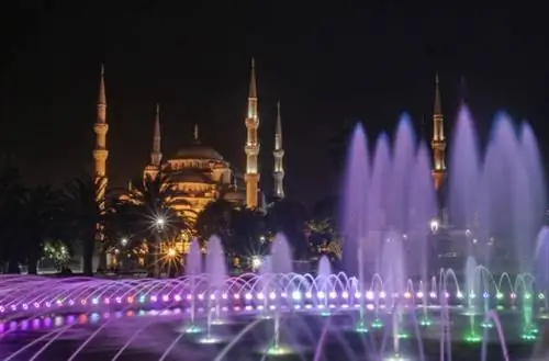 Красиво освещенный большой фонтан парка Султанахмет и Голубая мечеть вдалеке.