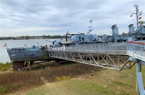USS Kidd сидит высоко и сухо во время необычно низкой реки Миссисипи в Батон-Руж, когда люди идут под эсминцем времен Второй мировой войны.