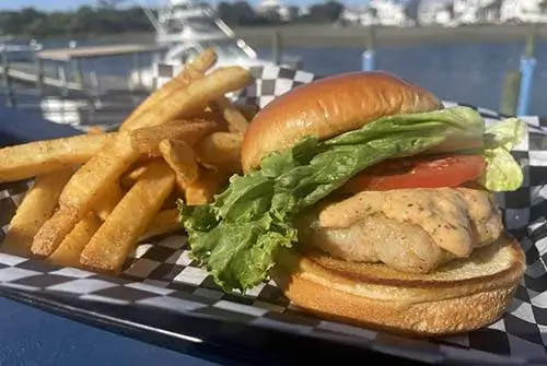 Насладитесь гамбургером из креветок с горячим хрустящим картофелем фри в ресторане Sharkys вдоль канала на пляже Оушен-Айл.