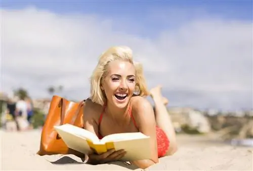 девушка смеется, читая на пляже