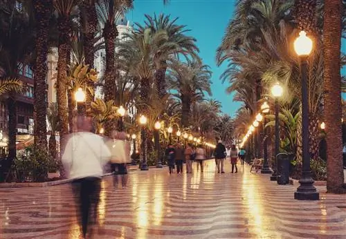 Вечерняя фотография Explanada de Alicante с включенными фонарными столбами и множеством прогуливающихся людей.