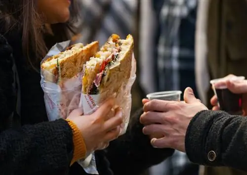 Женщина с двумя бутербродами из All'Antico Vinaio во Флоренции стоит рядом с мужчиной с чашкой кофе.