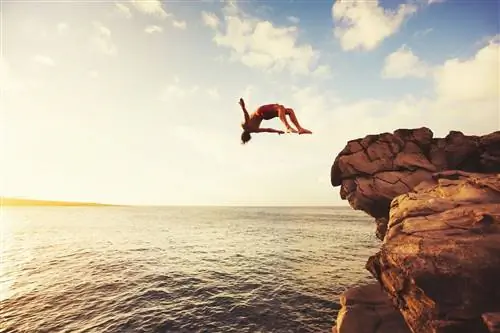 Мужчина прыгает со скалы в океан